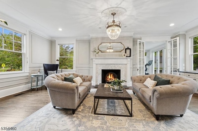 living area featuring wood finished floors, crown molding, a chandelier, a high end fireplace, and recessed lighting