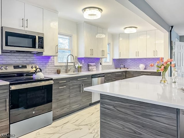 kitchen featuring decorative backsplash, appliances with stainless steel finishes, a sink, light countertops, and marble finish floor