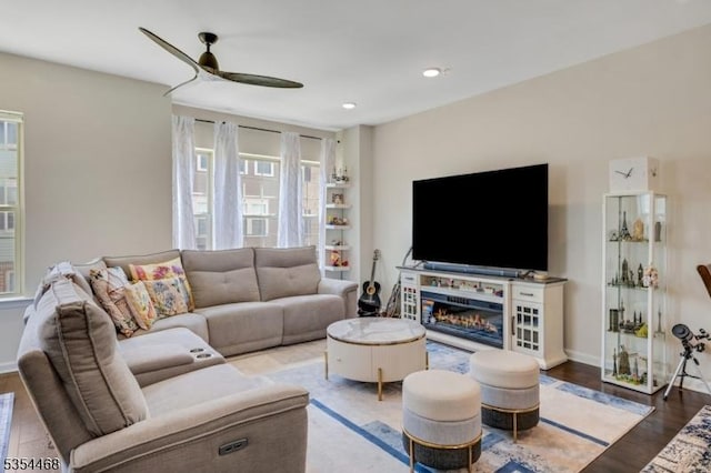 living area with a ceiling fan, baseboards, a glass covered fireplace, and wood finished floors