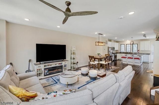 living area featuring recessed lighting, a ceiling fan, a glass covered fireplace, and dark wood-style floors