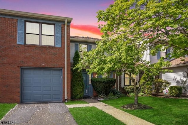 view of property with brick siding, an attached garage, a yard, and driveway
