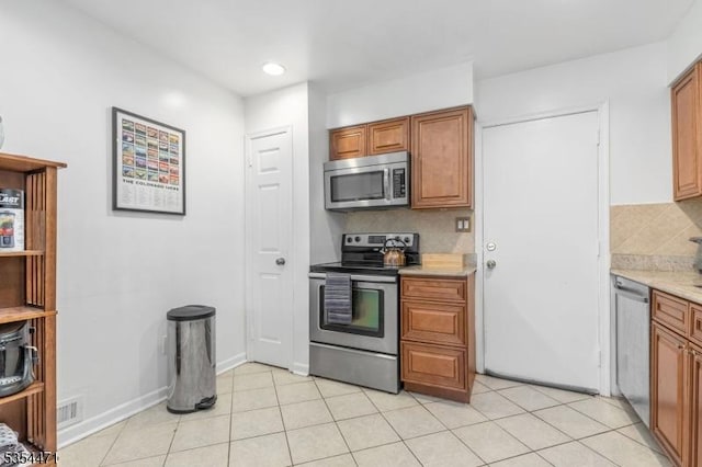 kitchen with light countertops, appliances with stainless steel finishes, brown cabinetry, and backsplash