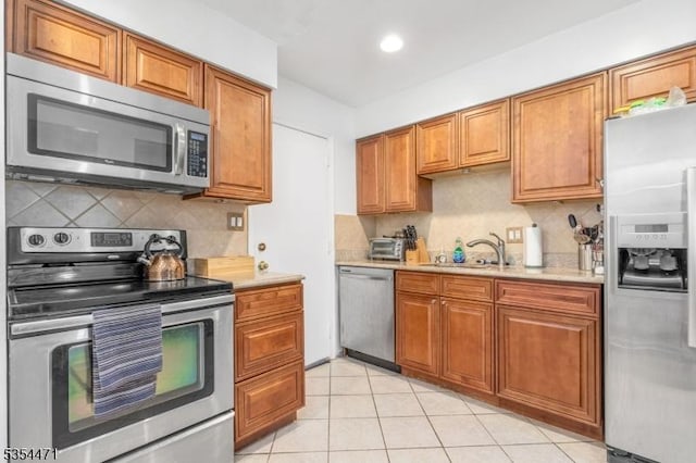 kitchen with brown cabinetry, tasteful backsplash, a sink, light countertops, and stainless steel appliances