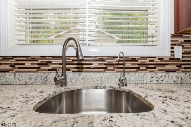 room details featuring light stone counters, a sink, decorative backsplash, and white cabinets