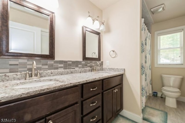 bathroom with baseboards, a sink, double vanity, and toilet