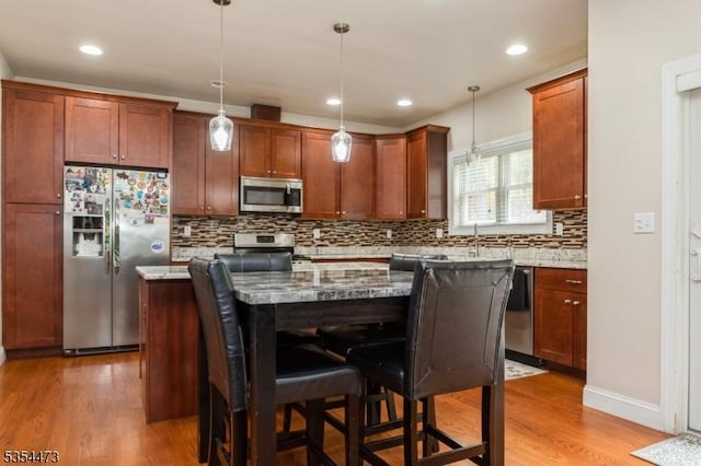 kitchen with backsplash, a kitchen bar, light stone counters, light wood-style floors, and stainless steel appliances