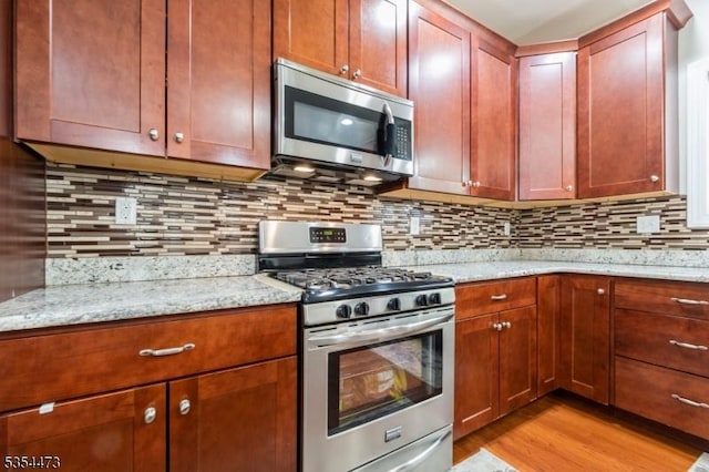 kitchen with tasteful backsplash, appliances with stainless steel finishes, light stone counters, and light wood-style flooring