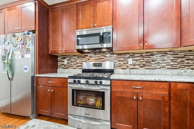 kitchen featuring light wood-type flooring, tasteful backsplash, light stone countertops, and stainless steel appliances