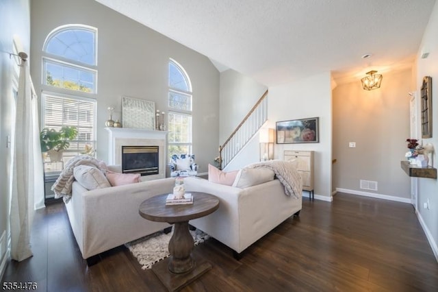 living room featuring an inviting chandelier, a glass covered fireplace, stairs, baseboards, and dark wood-type flooring