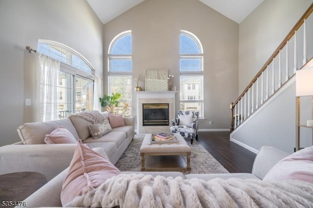 living room featuring high vaulted ceiling, a glass covered fireplace, baseboards, wood finished floors, and stairway