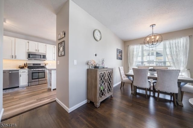 dining space with an inviting chandelier, a textured ceiling, baseboards, wood finished floors, and lofted ceiling