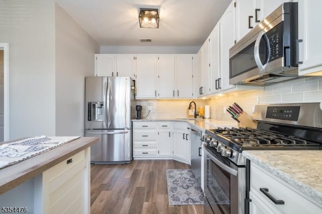 kitchen with white cabinets, light stone counters, a sink, dark wood finished floors, and stainless steel appliances