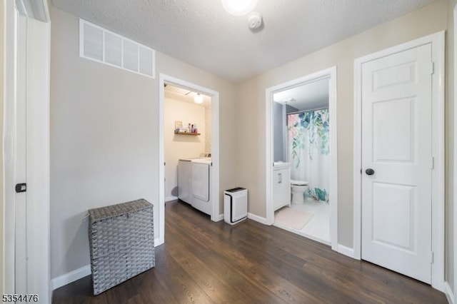 bedroom with visible vents, washing machine and dryer, dark wood finished floors, baseboards, and ensuite bath