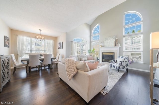 living area featuring dark wood-style flooring, a glass covered fireplace, a notable chandelier, and a healthy amount of sunlight
