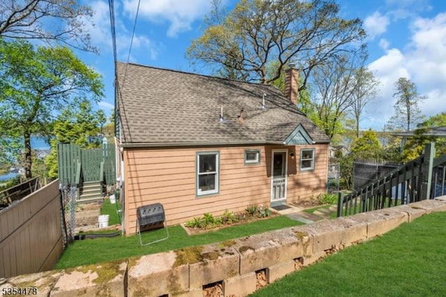 rear view of house featuring fence, a chimney, a yard, and a shingled roof