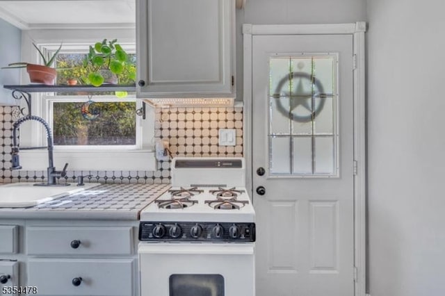 kitchen featuring backsplash, white gas stove, a sink, and light countertops