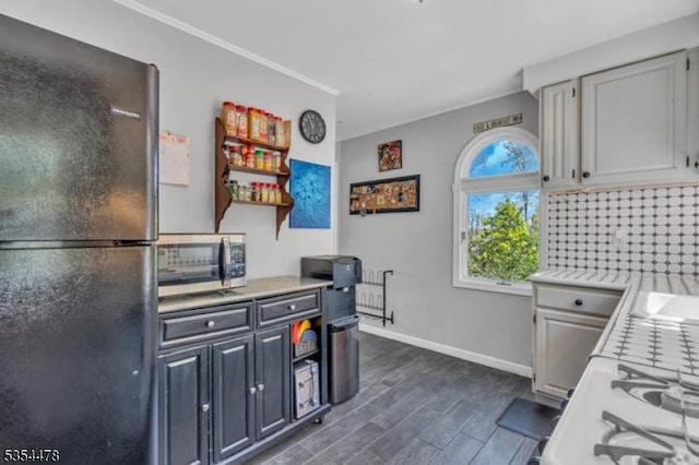 kitchen with freestanding refrigerator, open shelves, dark wood-type flooring, light countertops, and stainless steel microwave