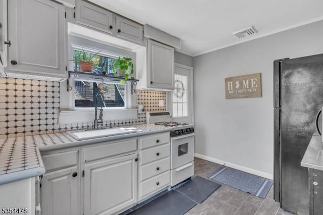 kitchen with decorative backsplash, white gas stove, a sink, light countertops, and freestanding refrigerator