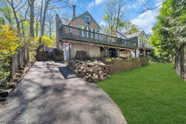 rear view of property with fence, aphalt driveway, a wooden deck, a chimney, and a yard