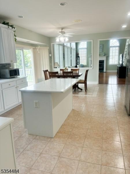 kitchen featuring white cabinetry, stainless steel microwave, light tile patterned floors, and ceiling fan