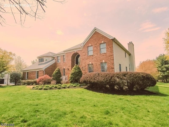 traditional-style home with brick siding, a chimney, and a front yard