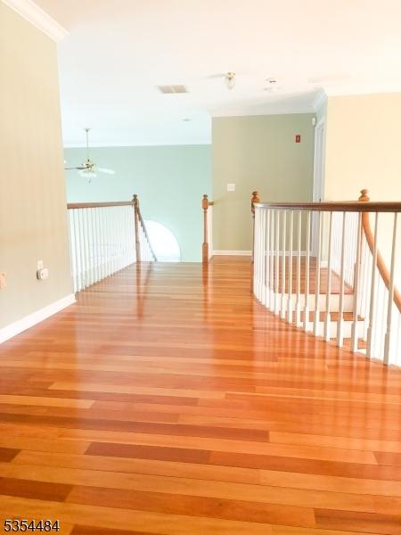 interior space featuring visible vents, crown molding, wood finished floors, baseboards, and an upstairs landing