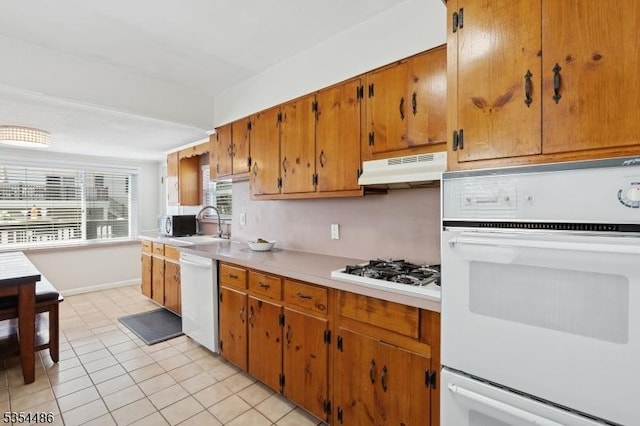 kitchen featuring brown cabinetry, light tile patterned flooring, white appliances, light countertops, and under cabinet range hood