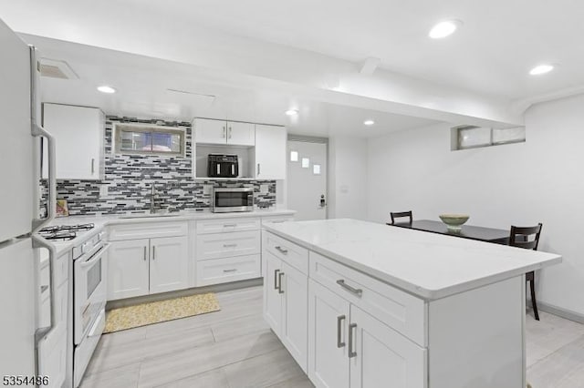 kitchen with white cabinets, a sink, white appliances, decorative backsplash, and a kitchen island