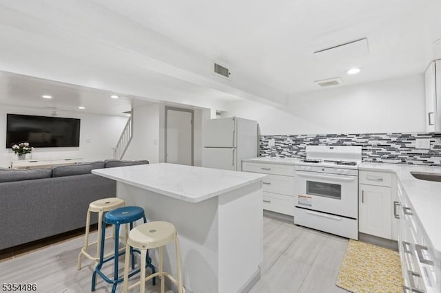 kitchen with white cabinets, white appliances, a breakfast bar area, decorative backsplash, and a kitchen island
