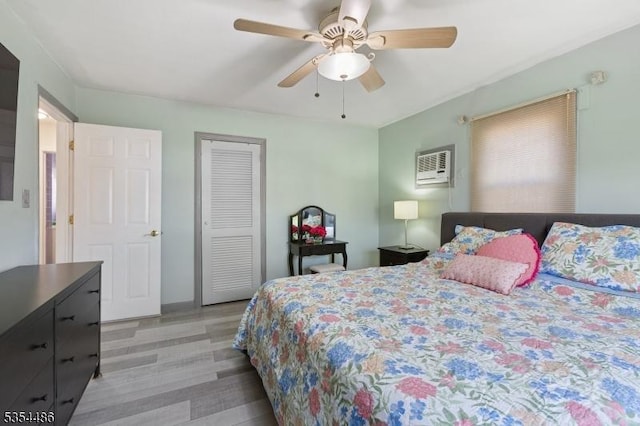bedroom with light wood-type flooring, ceiling fan, a wall unit AC, and a closet