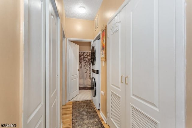 hall with visible vents, stacked washer and dryer, a textured ceiling, and light wood-style flooring
