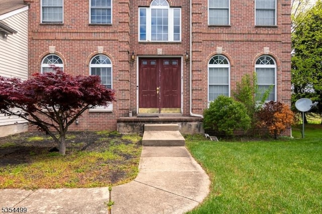view of exterior entry with brick siding and a lawn