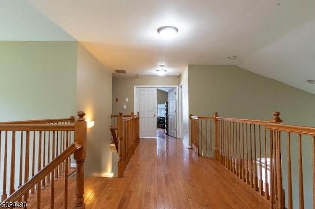 hall with wood-type flooring, an upstairs landing, lofted ceiling, and visible vents