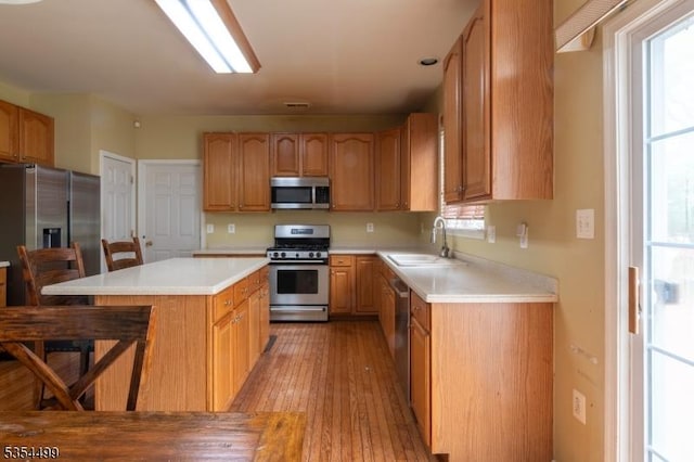 kitchen with a center island, a sink, light countertops, light wood finished floors, and stainless steel appliances