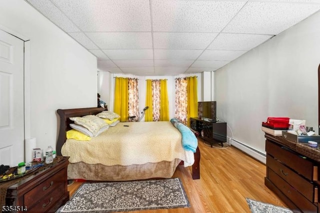 bedroom with light wood-style floors, a baseboard radiator, and a drop ceiling