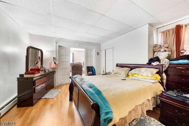 bedroom featuring light wood-style floors, baseboard heating, and a drop ceiling