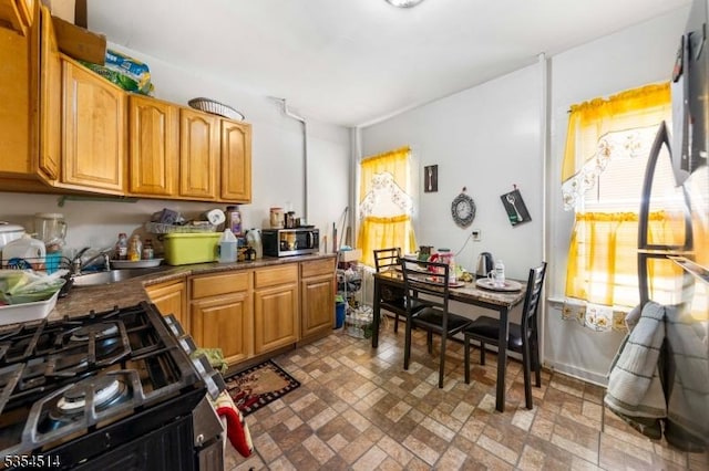 kitchen featuring a sink, stainless steel microwave, brick patterned floor, and gas stove