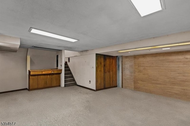finished basement with wooden walls, stairway, and light colored carpet