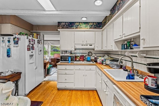 kitchen with a sink, light countertops, stainless steel microwave, white fridge with ice dispenser, and under cabinet range hood