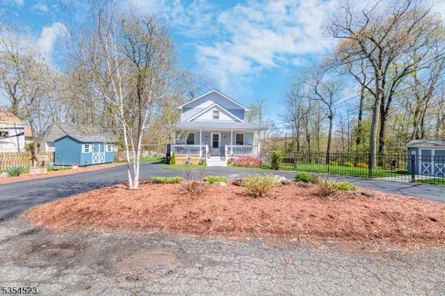 bungalow-style home with an outdoor structure, fence, covered porch, and driveway