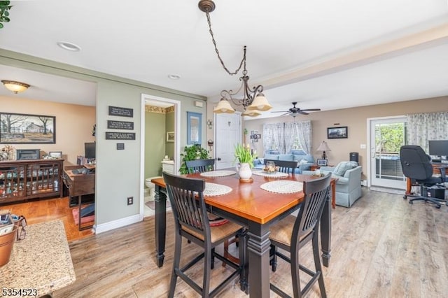 dining room with baseboards, light wood-style flooring, and ceiling fan with notable chandelier