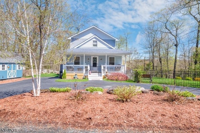 bungalow-style home with fence, a storage unit, an outdoor structure, aphalt driveway, and covered porch