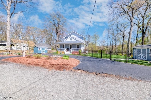 bungalow-style home featuring fence, a porch, a shed, an outbuilding, and driveway