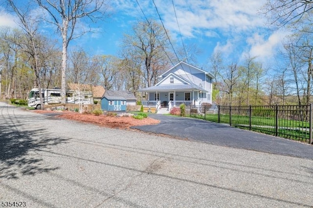 view of front facade with fence, covered porch, and aphalt driveway