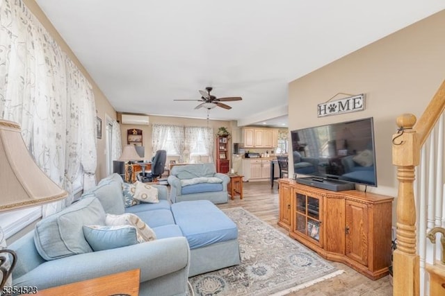 living room featuring light wood-type flooring, ceiling fan, a wall mounted AC, and stairway