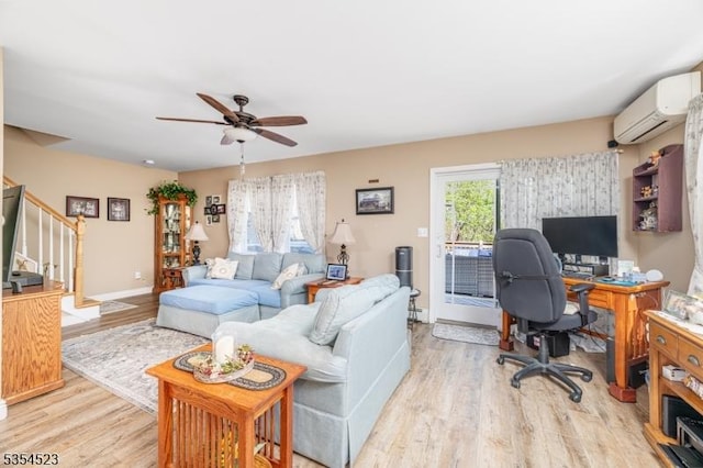 living area with stairs, an AC wall unit, ceiling fan, and light wood-style flooring