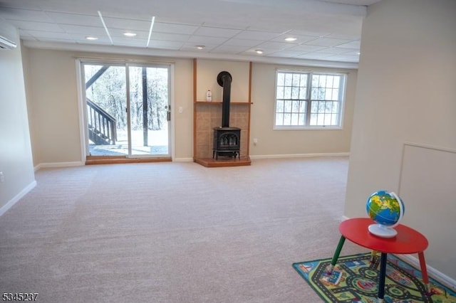 unfurnished living room featuring baseboards, a wood stove, carpet flooring, and a paneled ceiling