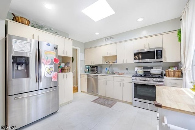 kitchen with visible vents, white cabinets, a sink, a skylight, and stainless steel appliances