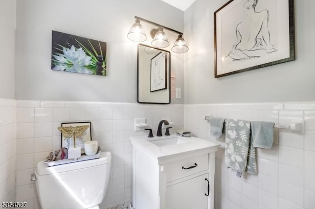 bathroom featuring vanity, wainscoting, toilet, and tile walls