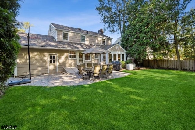 back of property with a lawn, a patio area, fence, and a chimney